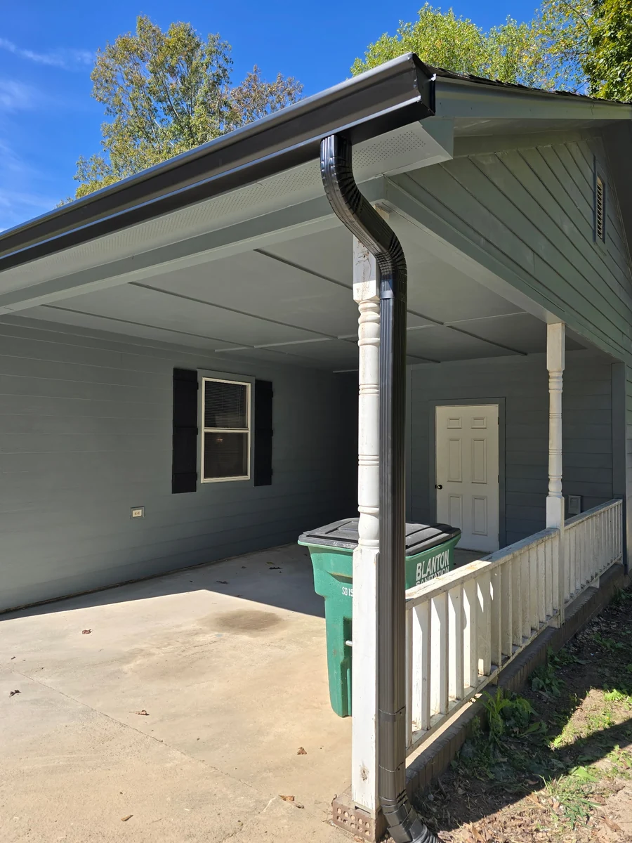 Completed black gutter and downspout on a covered porch