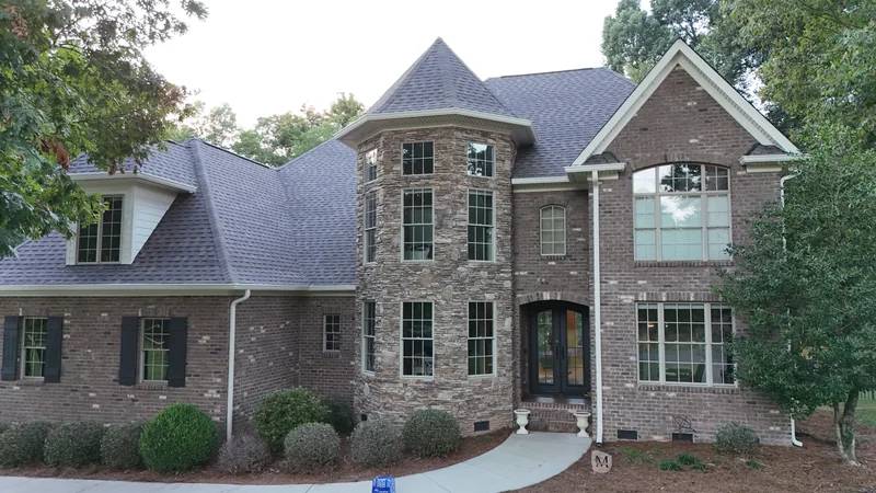 Brick and stone home with a turret and multiple gray shingle rooflines