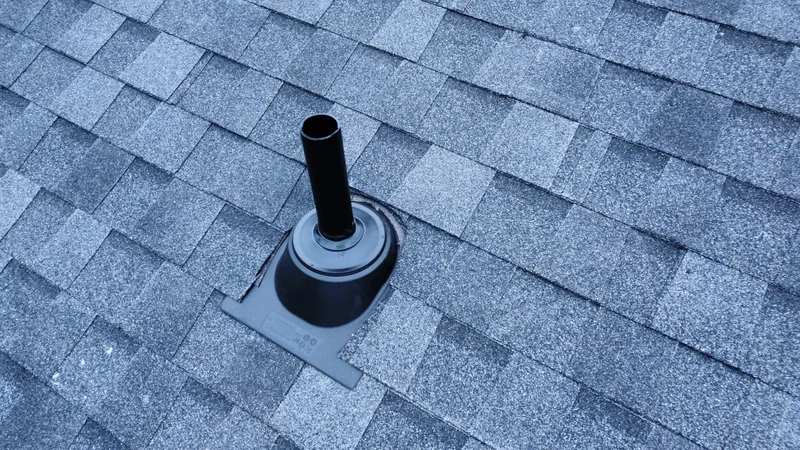 Close view of a black vent pipe and flashing boot on gray shingles